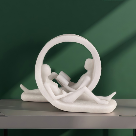 Бяла статуетка на двама души, четящи книги в легнало положение вътре в декоративен кръг