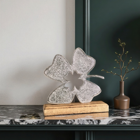 Сребриста метална статуетка във формата на четирилистна детелина с текстурирана повърхност върху дървена основа