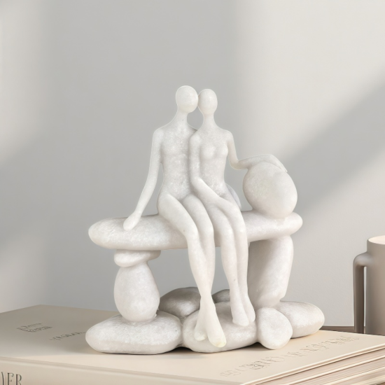 Бяла статуетка на влюбена двойка, седяща прегърната върху каменна пейка