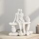 Бяла статуетка на влюбена двойка, седяща прегърната върху каменна пейка
