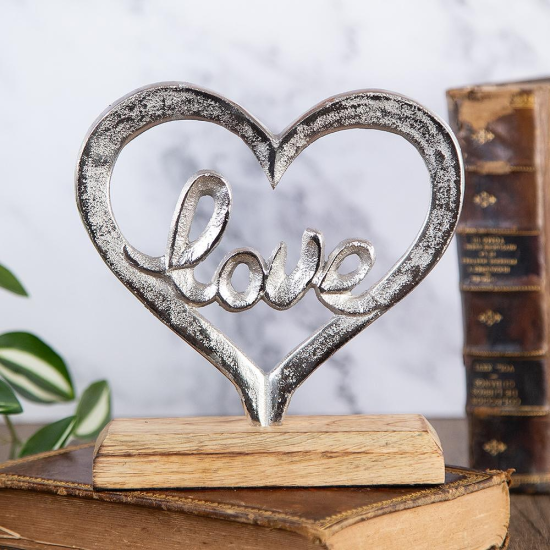 Статуетка във формата на сърце от сребрист метал с надпис "Love" в средата, поставена на дървена основа