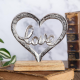 Статуетка във формата на сърце от сребрист метал с надпис "Love" в средата, поставена на дървена основа