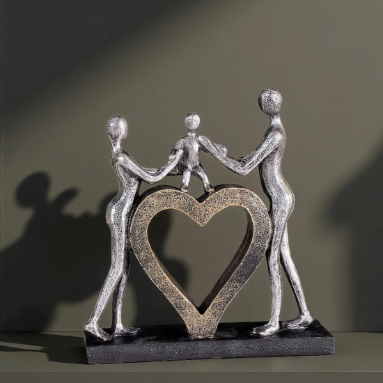 Сребриста статуетка на родители, държащи за ръце дете, което е стъпило върху голямо златно сърце