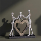 Сребриста статуетка на родители, държащи за ръце дете, което е стъпило върху голямо златно сърце