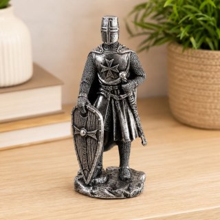 Фронтално поставена статуетка на рицар със щит върху светло бюро до книги и саксийно растение